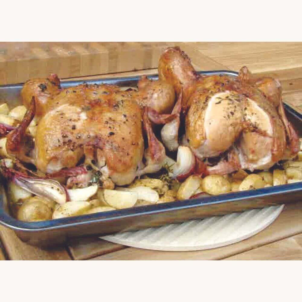 Two roasted chickens in a baking tray surrounded by roasted potatoes and onions, placed on a wooden surface.