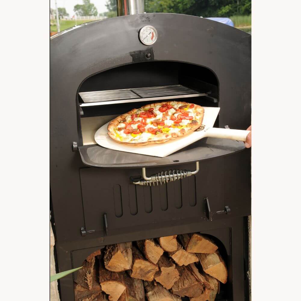 Tuscan Chef Medium Portable Family Pizza Oven with Cart (Model GX-C2) – A pizza being pulled from the oven with a wooden pizza peel, with firewood stored in the lower oven compartment.